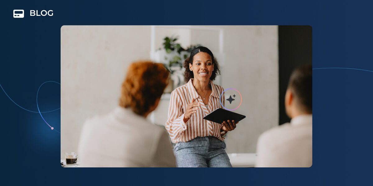 A woman holding a tablet smiles while discussing AI implementation with two people seated in front of her in a modern office setting, with "BLOG" displayed in the upper left corner of the blue border.