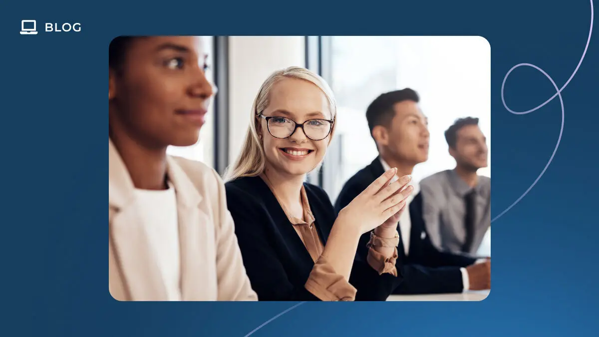 Four professionals sit in a row at a conference table. The woman in the center, wearing glasses and a black blazer, smiles at the camera while the others look forward attentively—a modern scene perfect for an Essential Guide to Customer Experience Metrics in 2025.