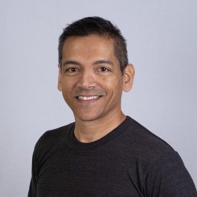 Smiling man with short dark hair wearing a dark t-shirt, posing in front of a plain light gray background—perfect for profiles of Customer Success professionals or CS Leaders in the AI industry.