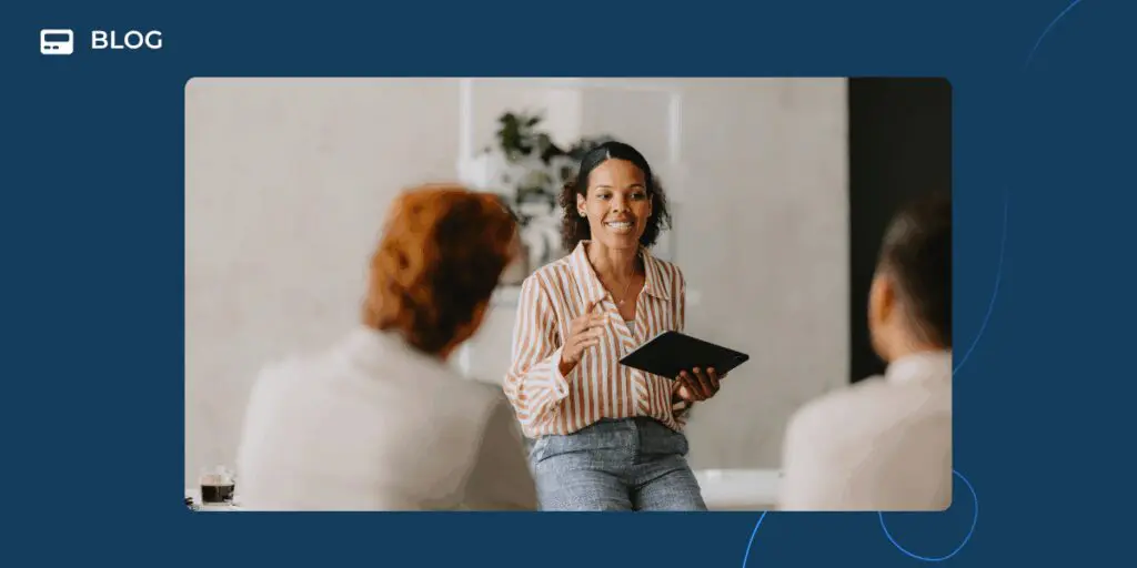 A woman holding a tablet smiles and speaks to two people in an office setting, highlighting AI Transformation. The image has a blue border and the word "BLOG" in the top left corner.