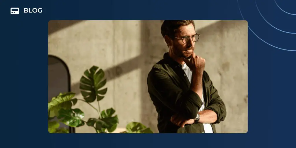 A man with glasses and a beard stands indoors, thoughtfully resting his chin on his hand as sunlight streams in, casting shadows on the wall and a large green plant nearby. "BLOG" appears in the upper left corner, hinting at insights for revenue teams or AI adoption.