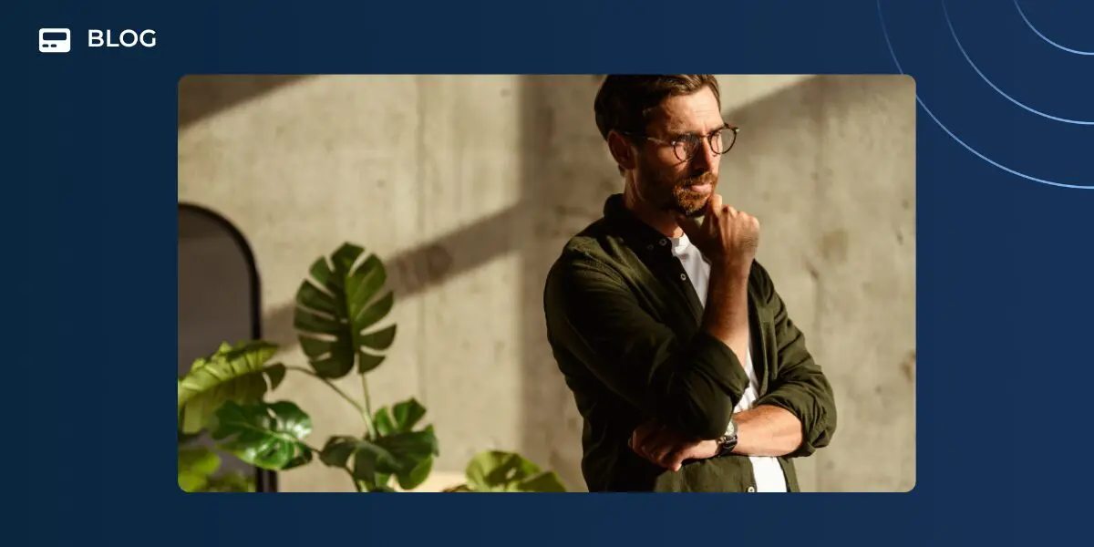 A man with glasses and a beard stands indoors, thoughtfully resting his chin on his hand as sunlight streams in, casting shadows on the wall and a large green plant nearby. "BLOG" appears in the upper left corner, hinting at insights for revenue teams or AI adoption.