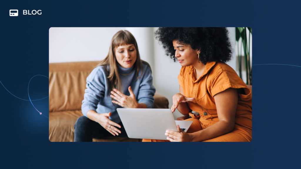 Two women sit together on a couch, focused on data displayed on a laptop screen. One gestures as they discuss strategies for Customer Success Teams, while the other listens attentively, holding a cup. The blue background is labeled "BLOG.
