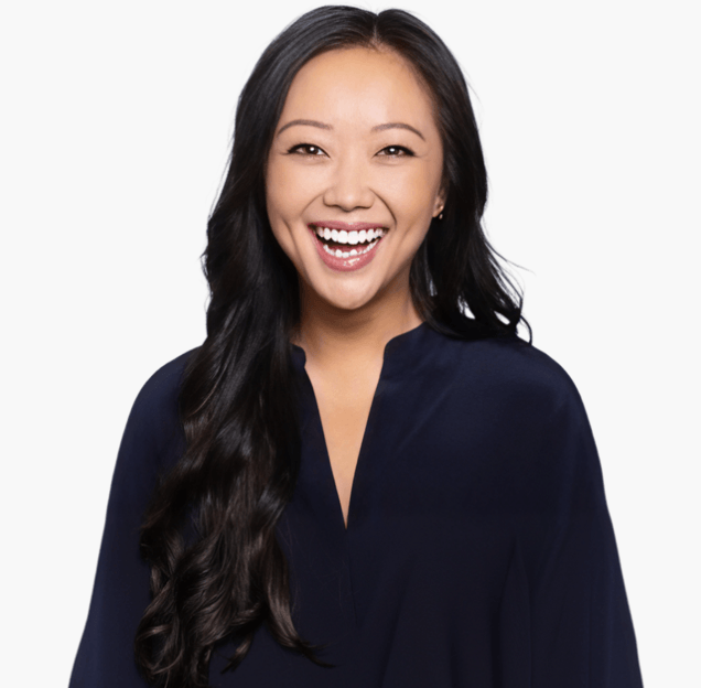 A woman with long black hair, wearing a dark blue top, smiles broadly and looks directly at the camera against a plain white background, embodying the spirit of AI adoption and innovation championed by OpenAI.