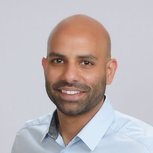 Adnan Rahman, one of the notable CS Leaders, is a man with a bald head and trimmed beard, smiling in a light blue collared shirt as he poses confidently in front of a plain, light-colored boardroom background.