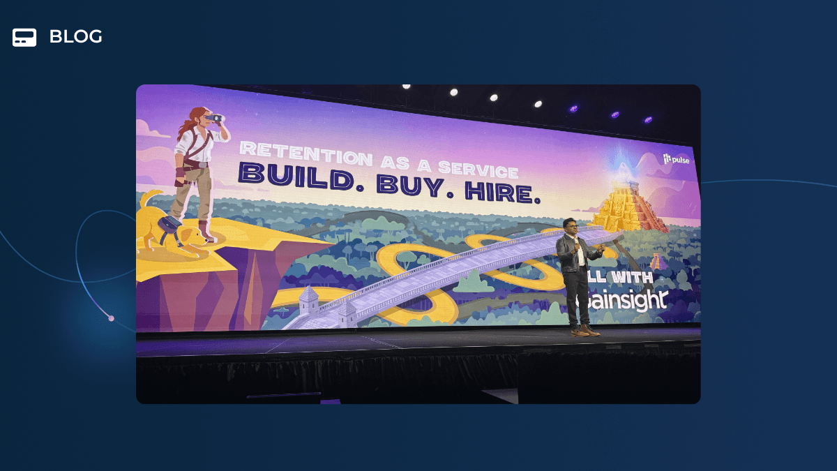 A person stands on stage in front of a large screen displaying "Retention as a Service: Build. Buy. Hire." with a cartoon scene of a woman looking at a golden temple and winding path—perfect for the Day One Recap at Pulse 2026.