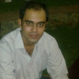 A man wearing glasses and a white shirt sits outdoors on the grass, looking at the camera with a relaxed, Vibe Coding energy.