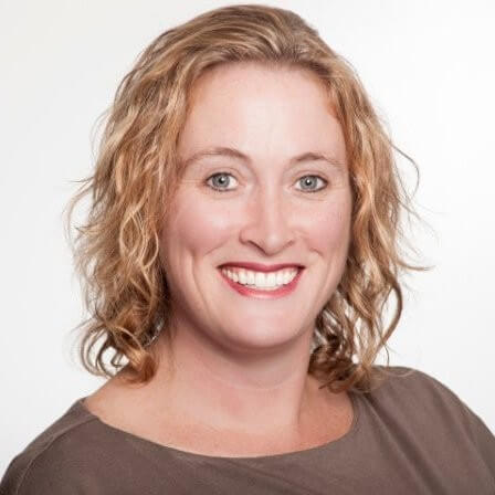 Smiling woman with wavy, shoulder-length blonde hair wearing a taupe top, pictured against a plain white background—her confident demeanor perfectly embodies the spirit of customer success.