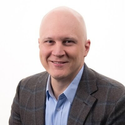 Bald man wearing a blue shirt and plaid blazer, smiling at the camera against a plain white background, representing the confidence that comes with fresh renewals.