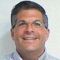 Tony Pante smiling wearing glasses and a striped collared shirt.