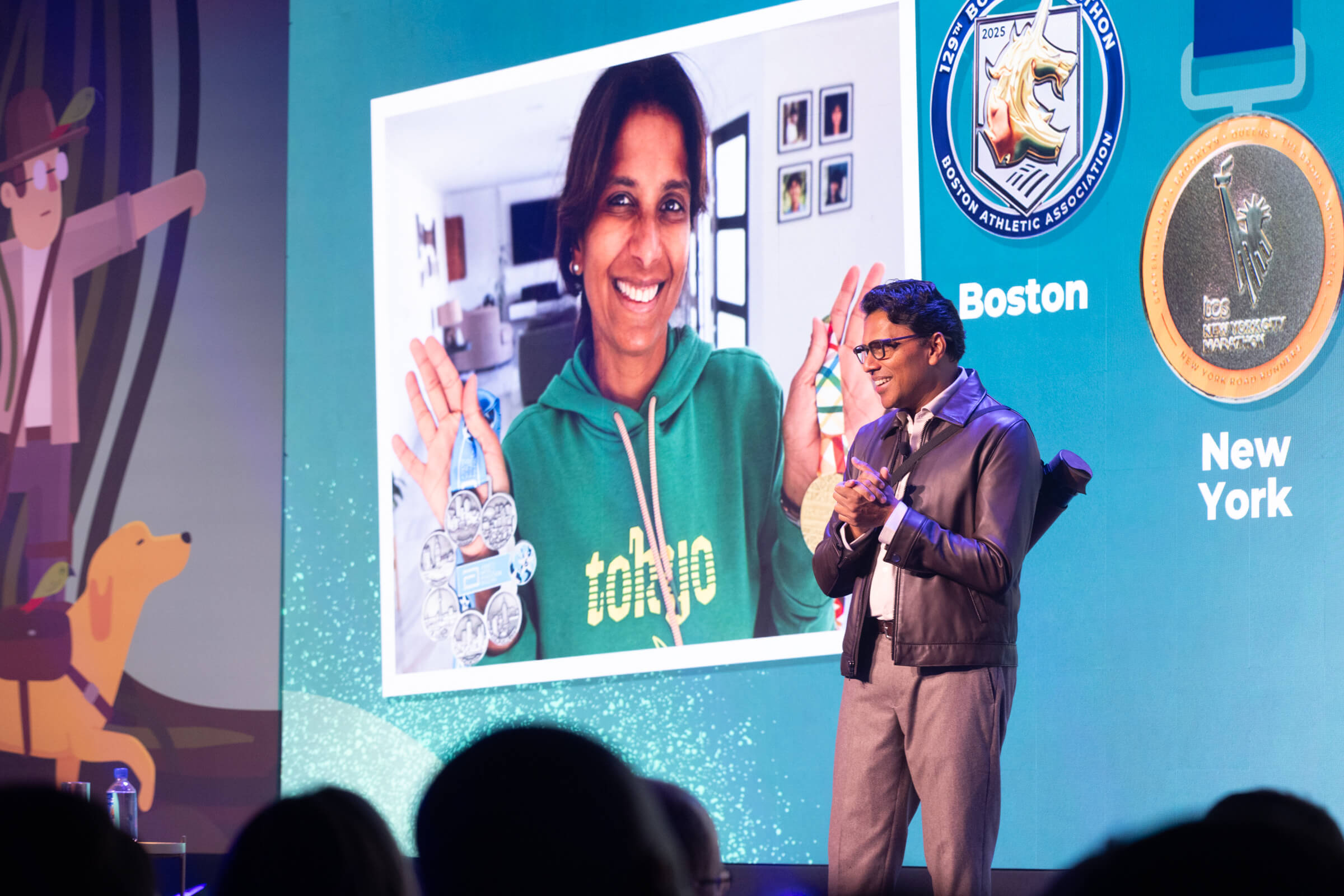 A man in a dark jacket stands on a stage at Pulse Europe 2026 in front of a large screen showing a smiling woman wearing a green hoodie and holding several marathon medals, illustrating a focus on retention.
