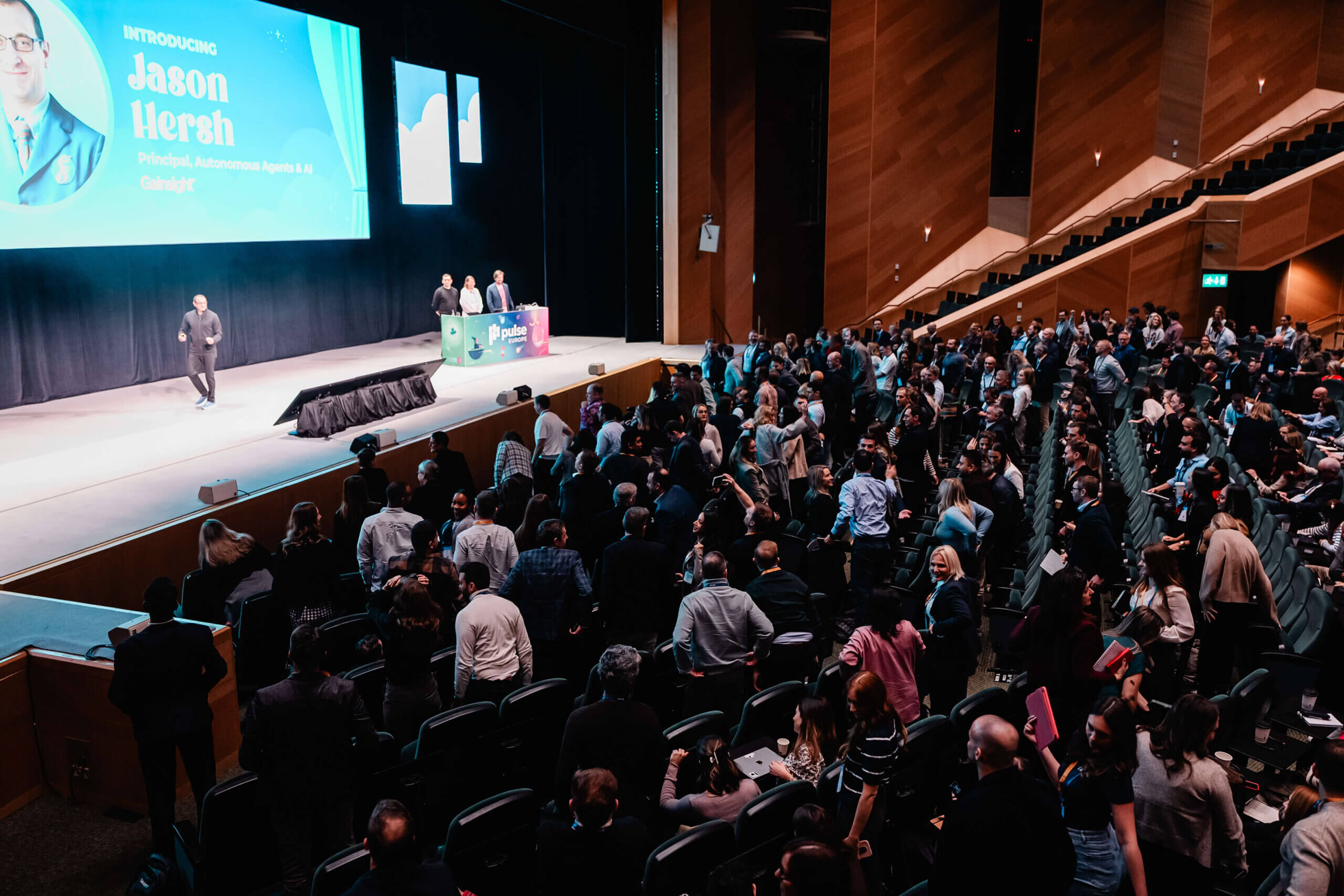 A speaker stands on stage at Pulse Europe 2026, addressing a large audience in a modern auditorium near a screen introducing Jason Hersh at the tech conference.