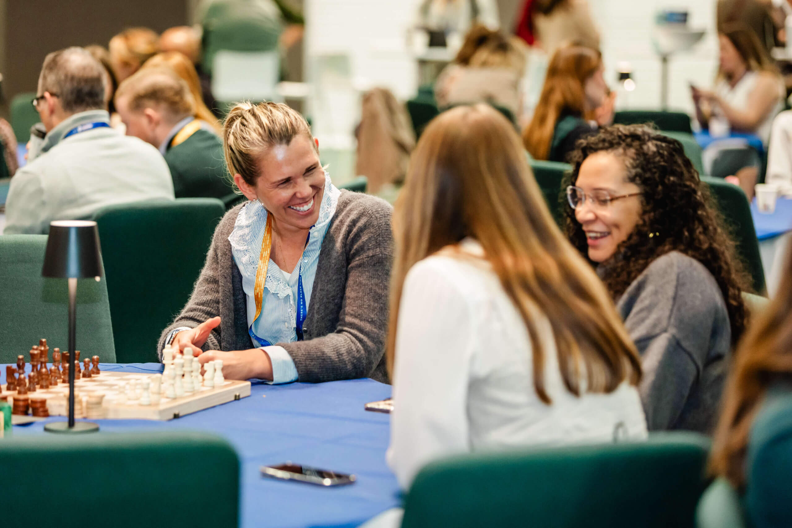 Three people laugh while seated at a table with a chessboard during a Pulse Europe 2026 tech conference.