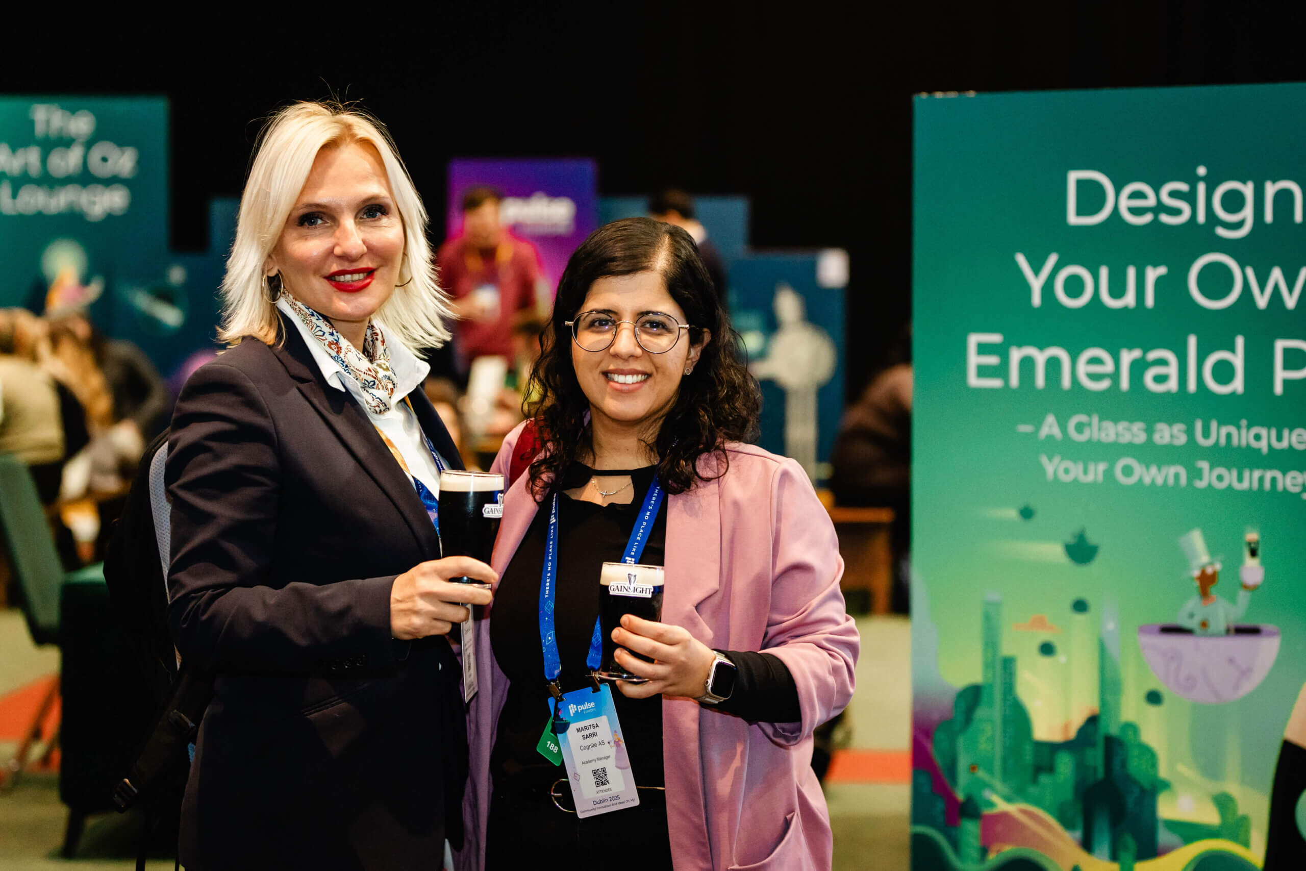 Two women stand together holding drinks and wearing conference badges at Pulse Europe 2026, with informational signs visible in the background.