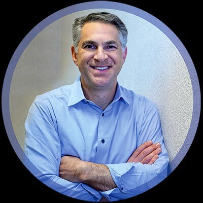 A CFO with short graying hair smiling with his arms crossed, wearing a light blue button-down shirt.